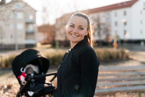 Leende kvinna ute på promenad med barnvagn i kvällssol